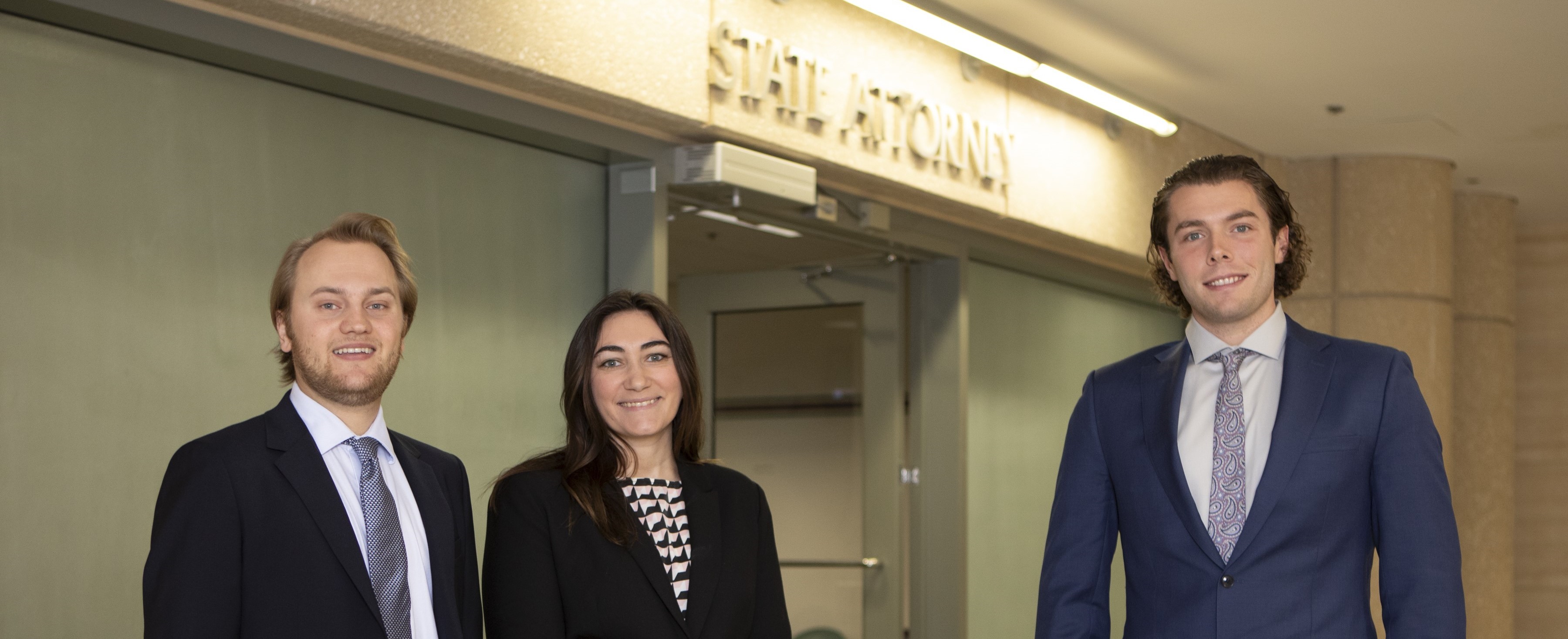 Student participant in clinic program stands next to two mentors in office hallway